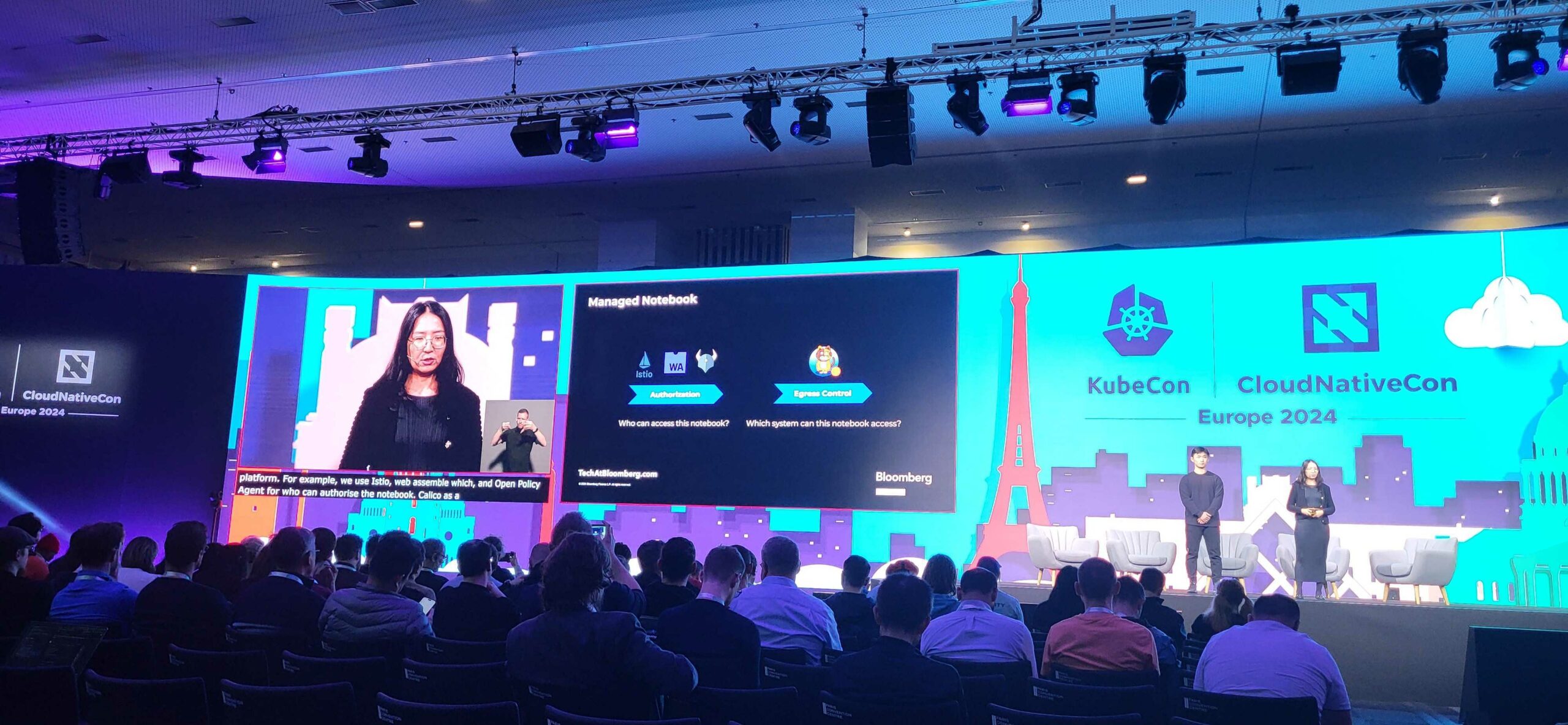 A large screen at KubeCon CloudNativeCon Europe 2024 shows a presentation about managed notebooks, with audience members watching