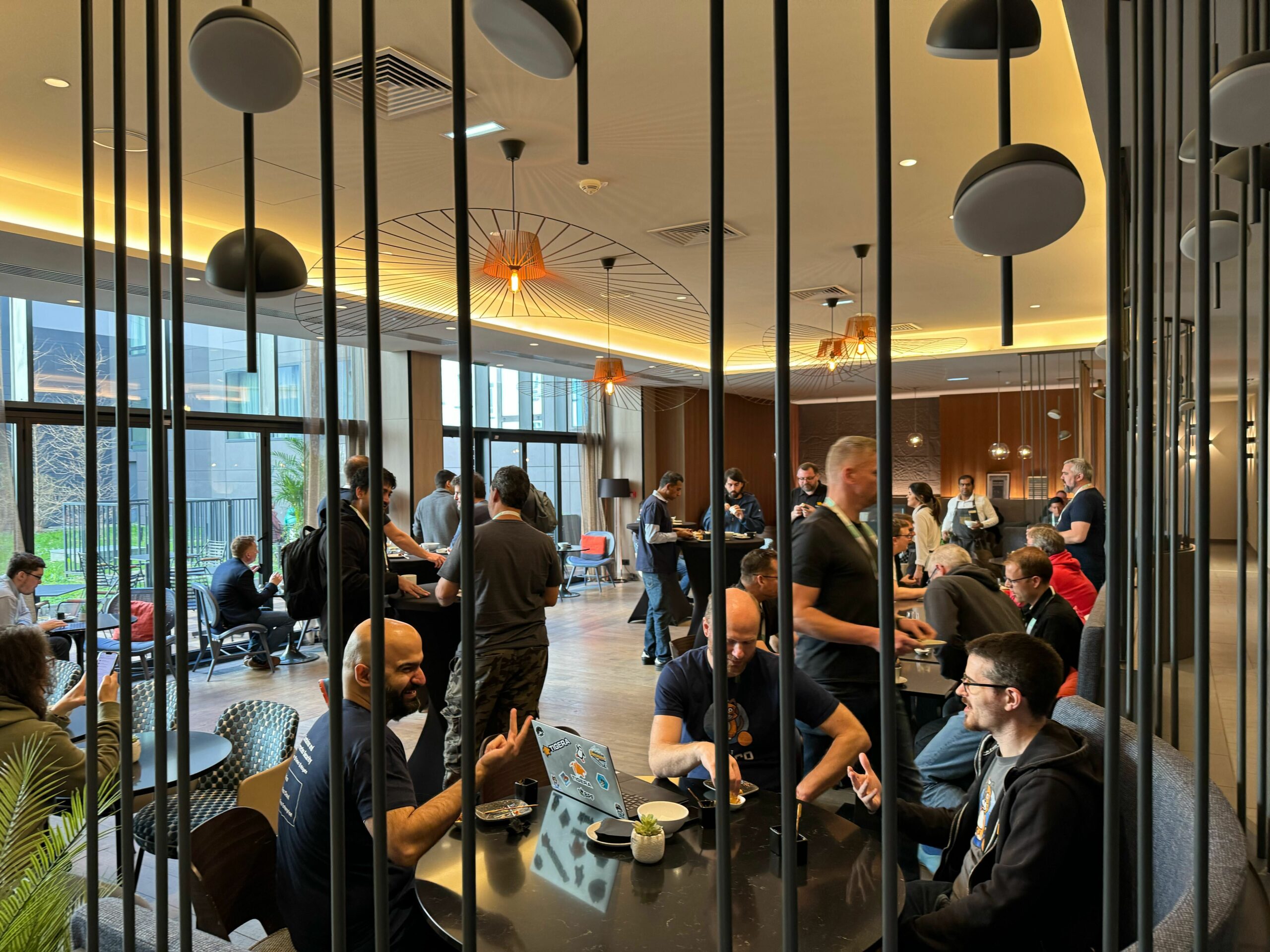 A view through a room divider shows many people socializing and working at tables in a modern, brightly lit room
