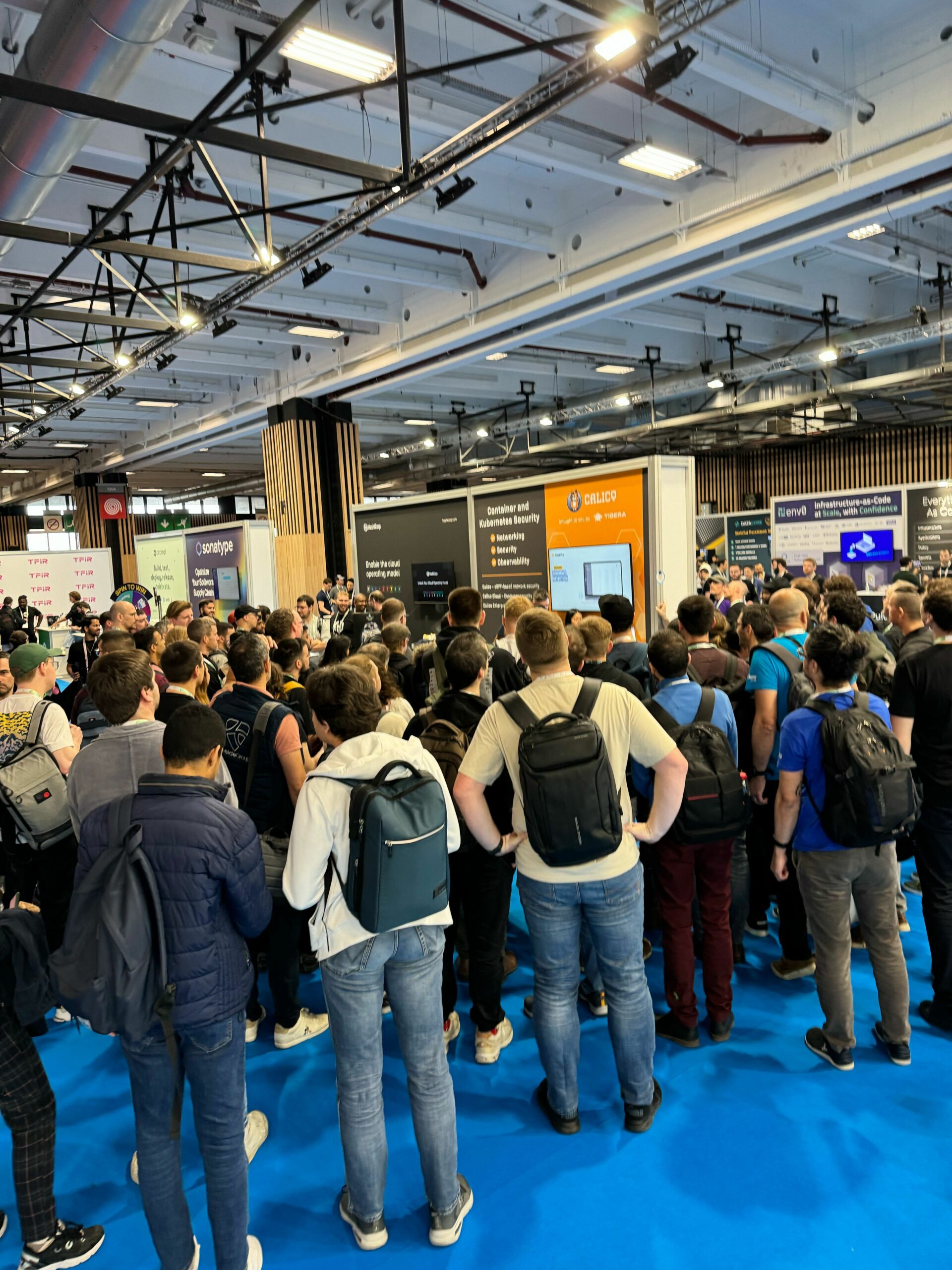 A large crowd of people at a the conference gathers around several booths displaying information on Calico