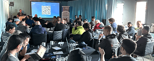 Audience watches a speaker presenting with a QR code on the screen.